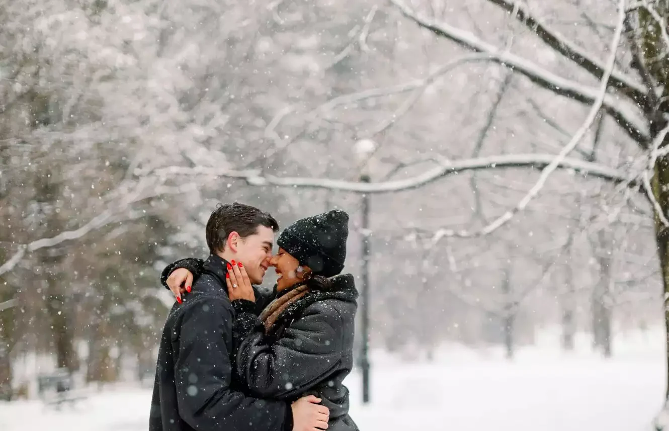 Engaged couple sharing a kiss in the snow during holiday engagement season.