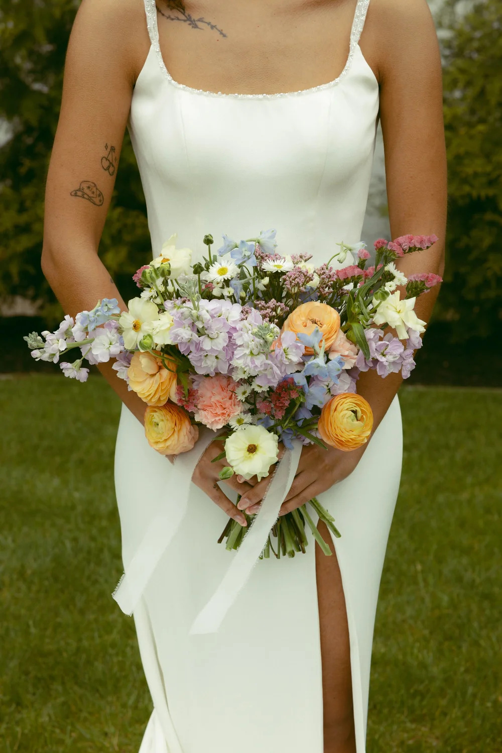 Bride holding a colorful spring wedding bouquet with ranunculus, delphinium, and pastel florals at a Southwest Michigan wedding planned by Forever & Always Event Planning