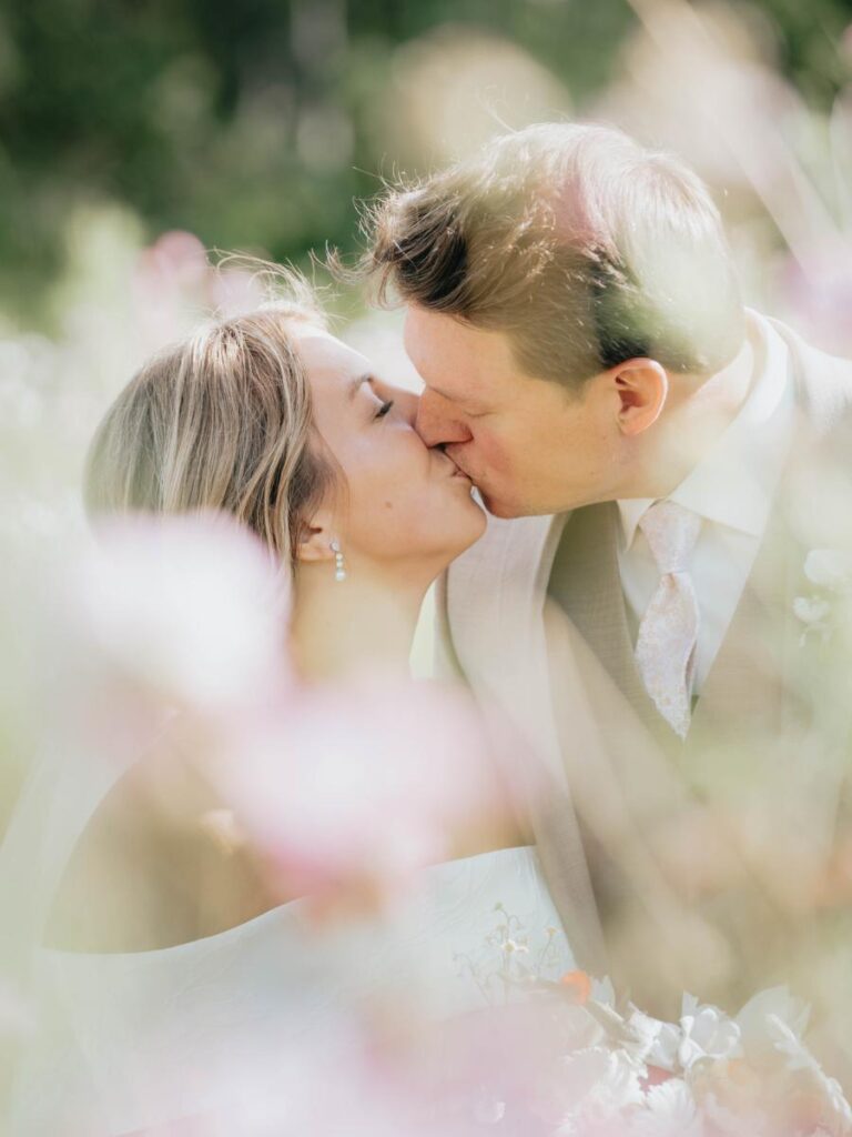 Close-up of bride and groom kissing surrounded by soft flowers and natural light