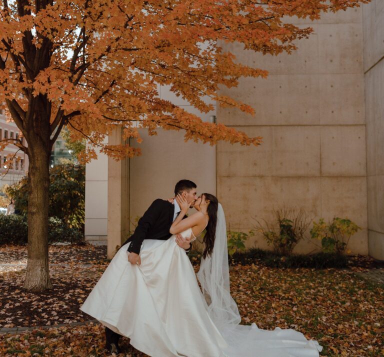 Bride and groom sharing a kiss beneath a vibrant orange autumn tree during an intimate downtown Grand Rapids elopement.