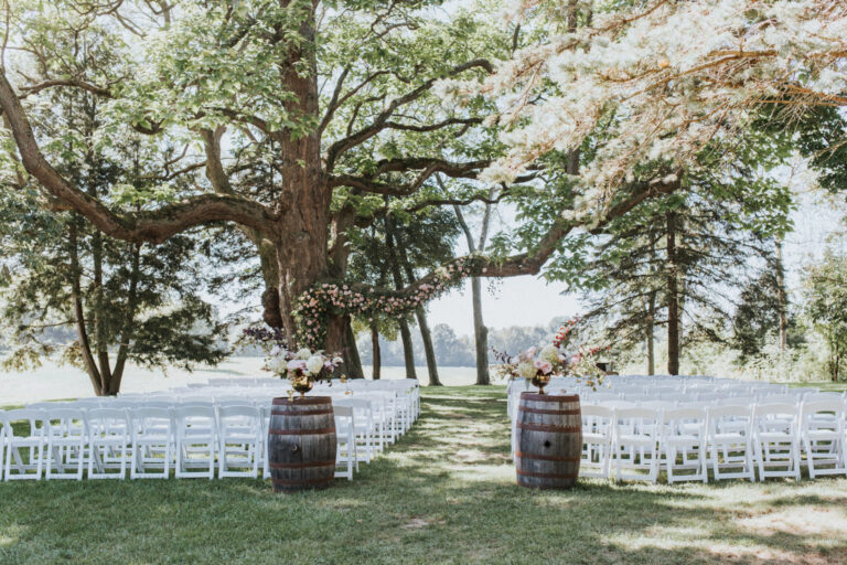 Outdoor waterfront wedding ceremony in Michigan with white chairs, floral arrangements and a flower-covered tree