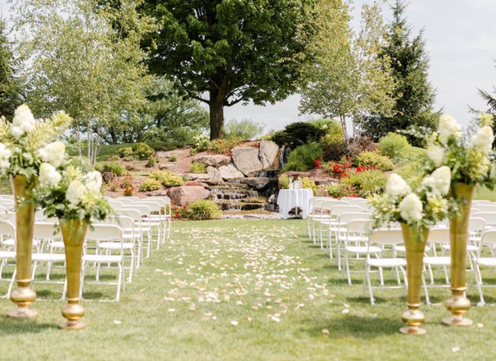 Outdoor summer wedding ceremony in Michigan with white chairs, floral arrangements and a garden waterfall