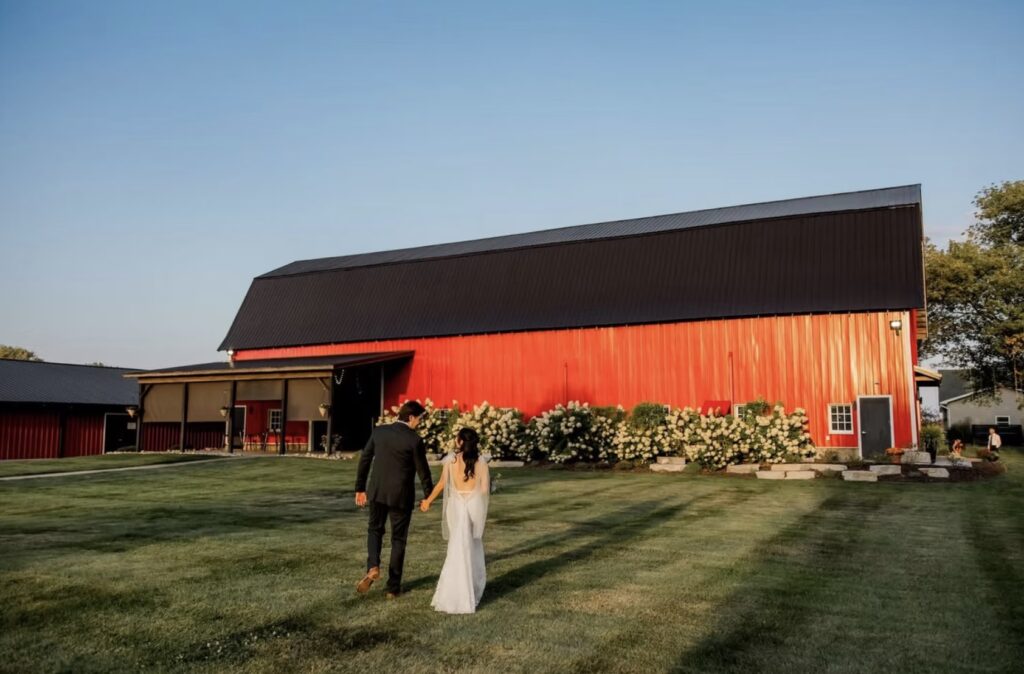Bride and groom walking toward a red barn at a summer wedding in Michigan