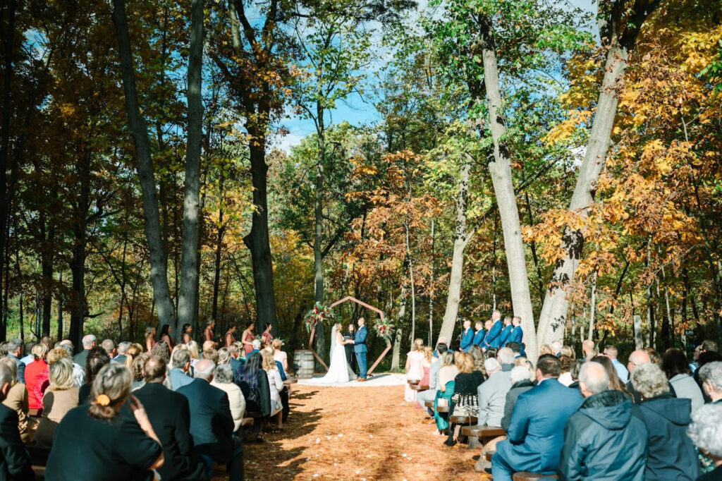 Outdoor fall wedding ceremony in a wooded West Michigan setting surrounded by colorful autumn foliage